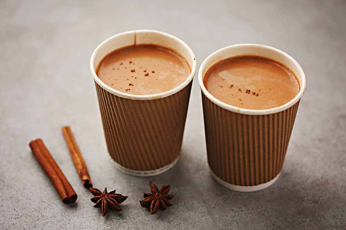 two cups filled with brown chai drink and spices 