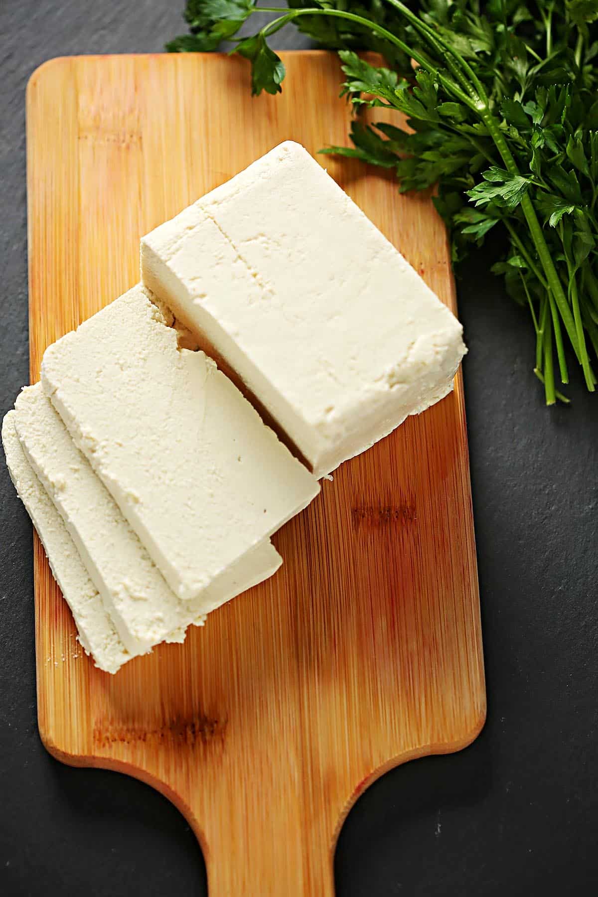 Wooden cutting board with sliced block of tofu. 