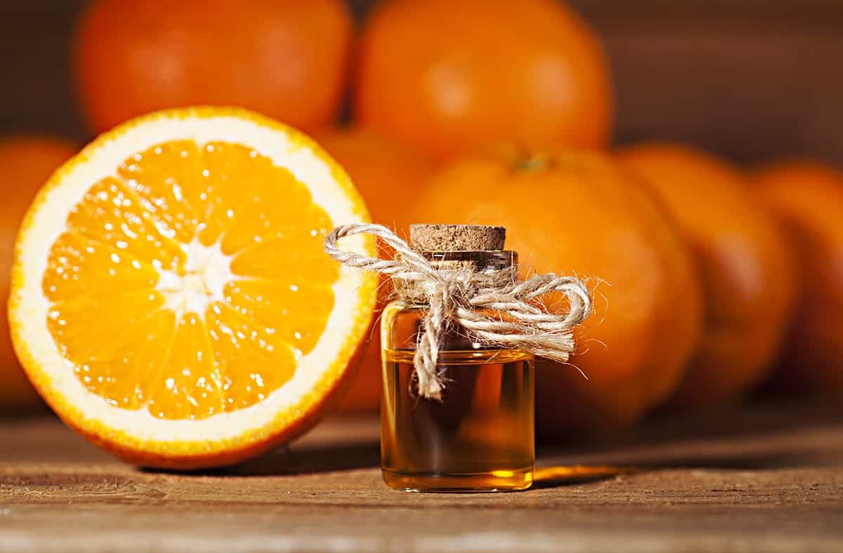 tabletop with glass bottle with orange blossom water and sliced orange. 