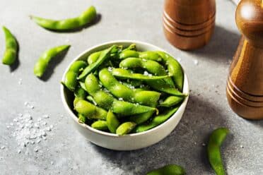 white bowl with green edamame sprinkled with salt.