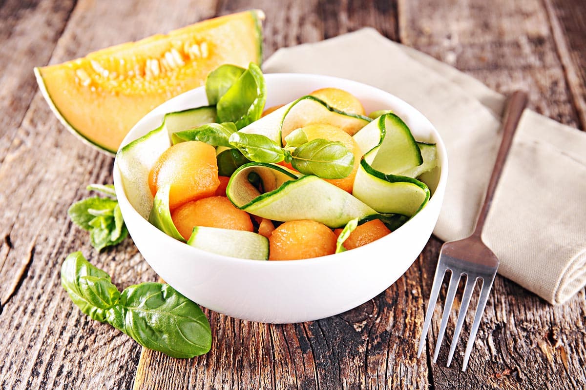 White bowl with salad made with honeydew melon, cucumber and fruit. 