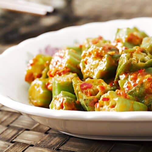White plate with cooked okra with red sauce.