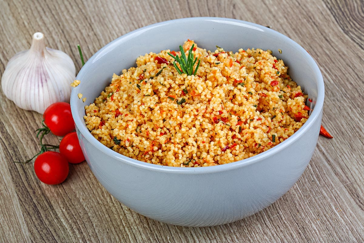 blue bowl with cooked couscous with tomatoes and garlic. 