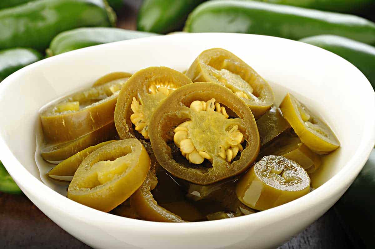 White bowl filled with sliced pickled green jalapeno peppers. 