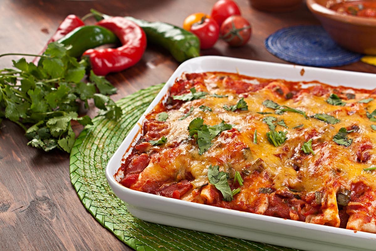 Dish with baked enchiladas topped with herbs. 