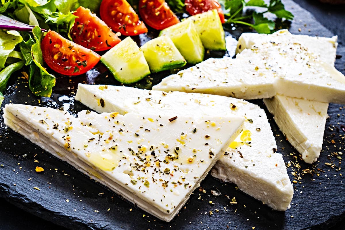 Sliced feta topped with olive oil and spices on top of the black plate. 
