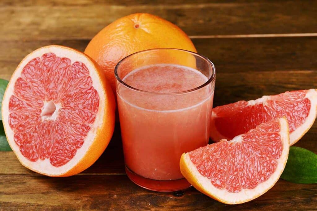 Sliced grapefruit and glass filled with grapefruit juice. 
