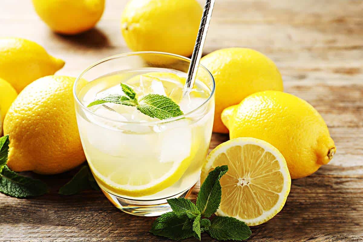 Glass filled with lemon juice with fresh lemons next to it. 