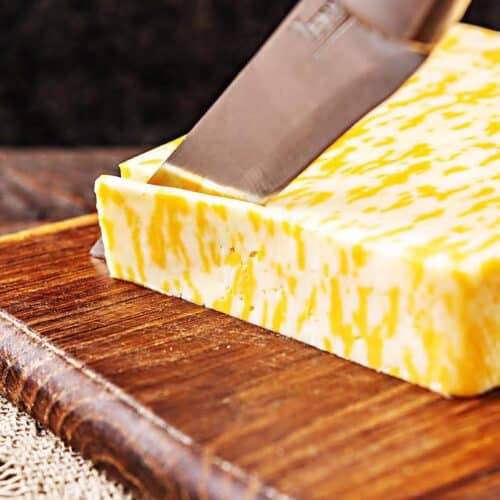 Block of Monterey Jack cheese on top of wooden cutting board.