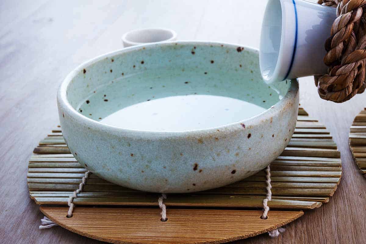 Bottle pouring sake to the ceramic white dish. 