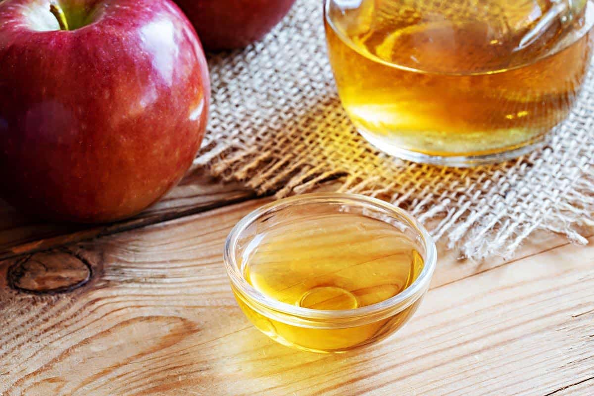 Small bowl filled with apple cider vinegar and apple in the background.