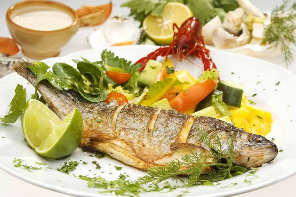 Serving plate with whole cooked fish and bright vegetables. 