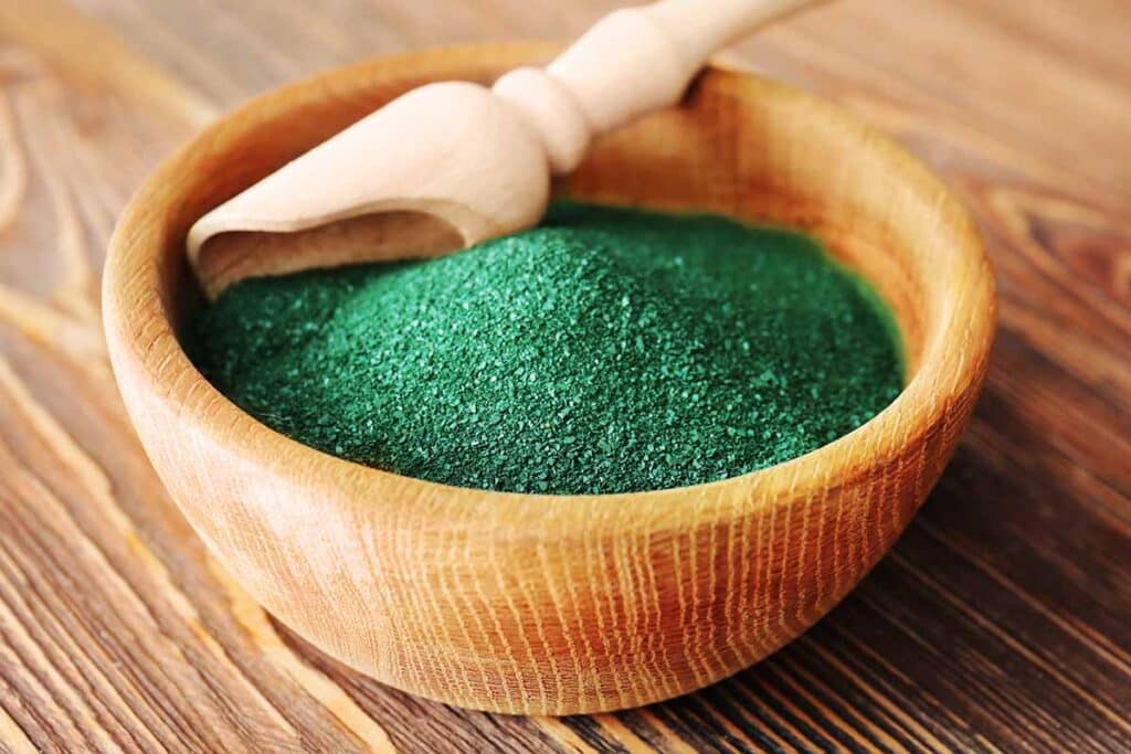 Wooden bowl filled with green spirulina powder. 