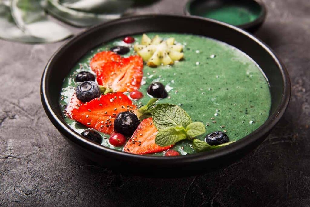 Green spirulina smoothie bowl topped with fresh fruits. 