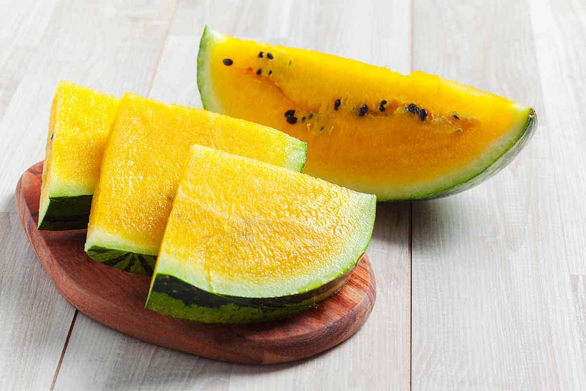 Sliced bright yellow watermelon served on top of the wooden serving board. 