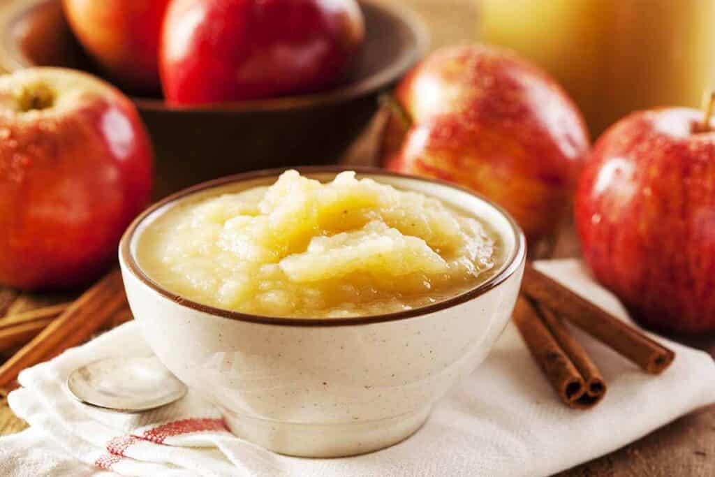 Small dish with applesauce next to fresh apples. 