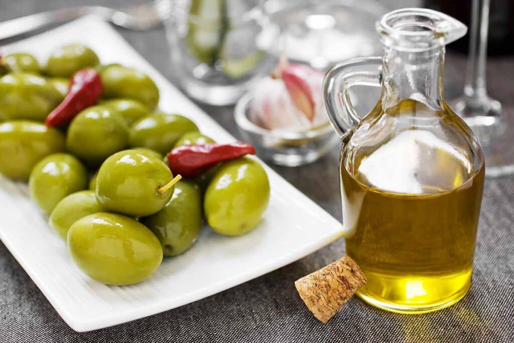Bottle with olive oil on the table, next to olives on the plate. 