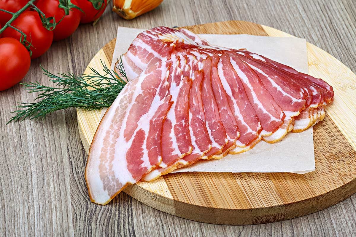 Slices of pork belly on the round cutting board. 