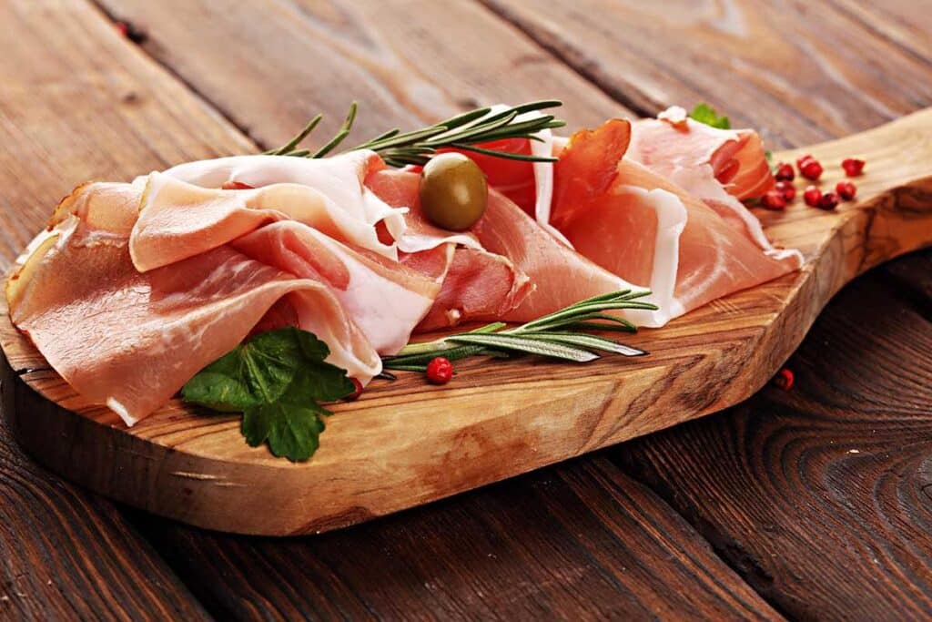 Thin slices of prosciutto on the round serving board with fresh herbs.