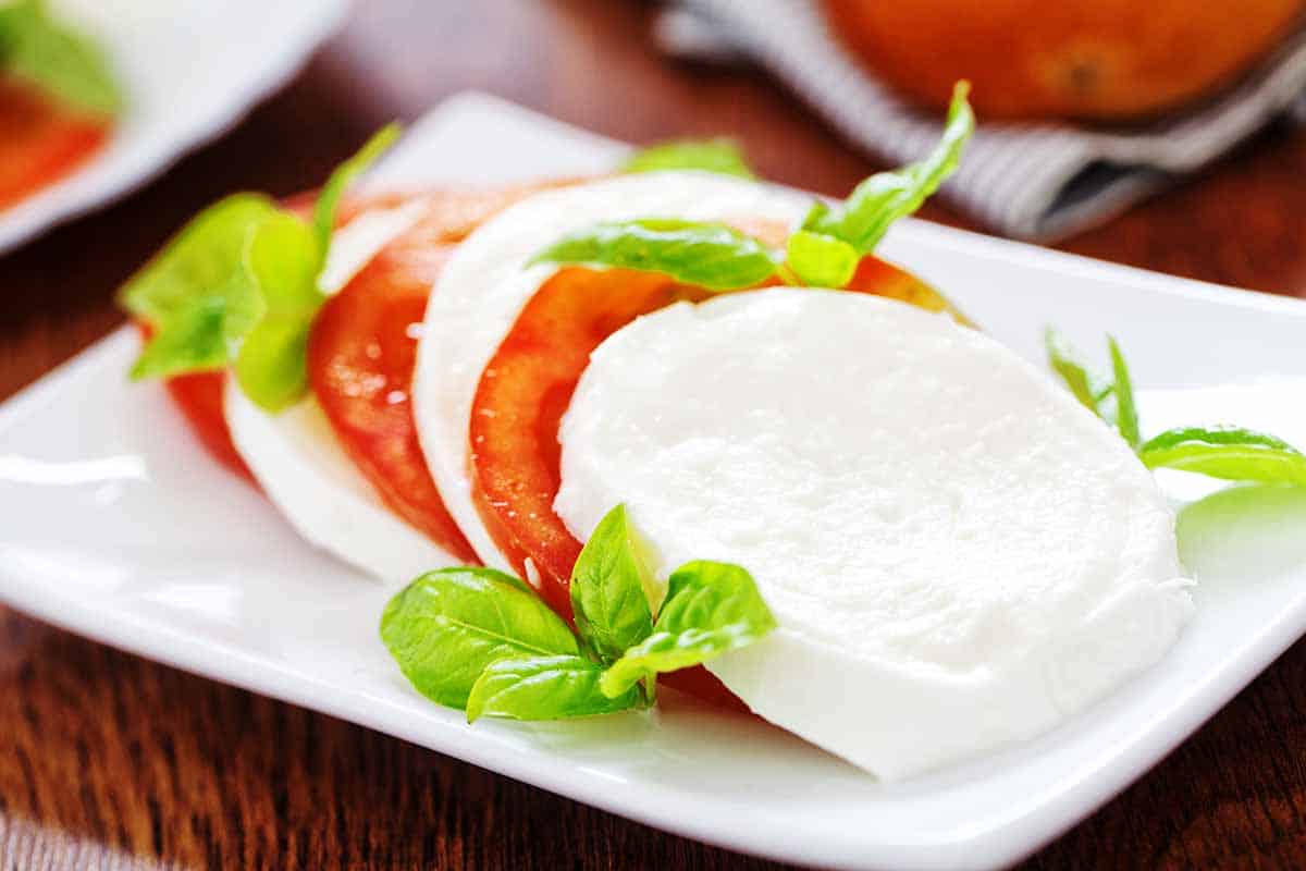 Sliced mozzarella with tomatoes served on the white plate. 