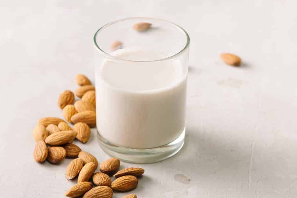 Glass filled with almond milk with nuts laying next to it. 