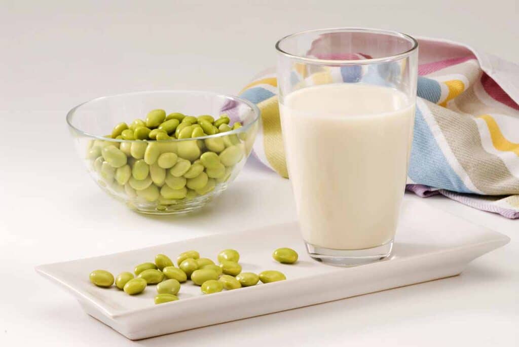 Glass with soy cream and edamame pods next to it. 