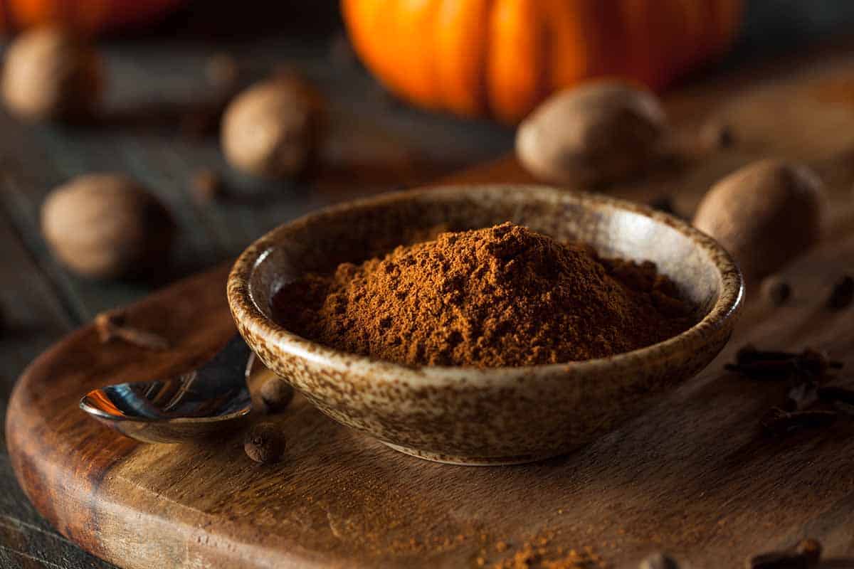 Small dish with pumpkin pie spice and whole pumpkin on the background. 