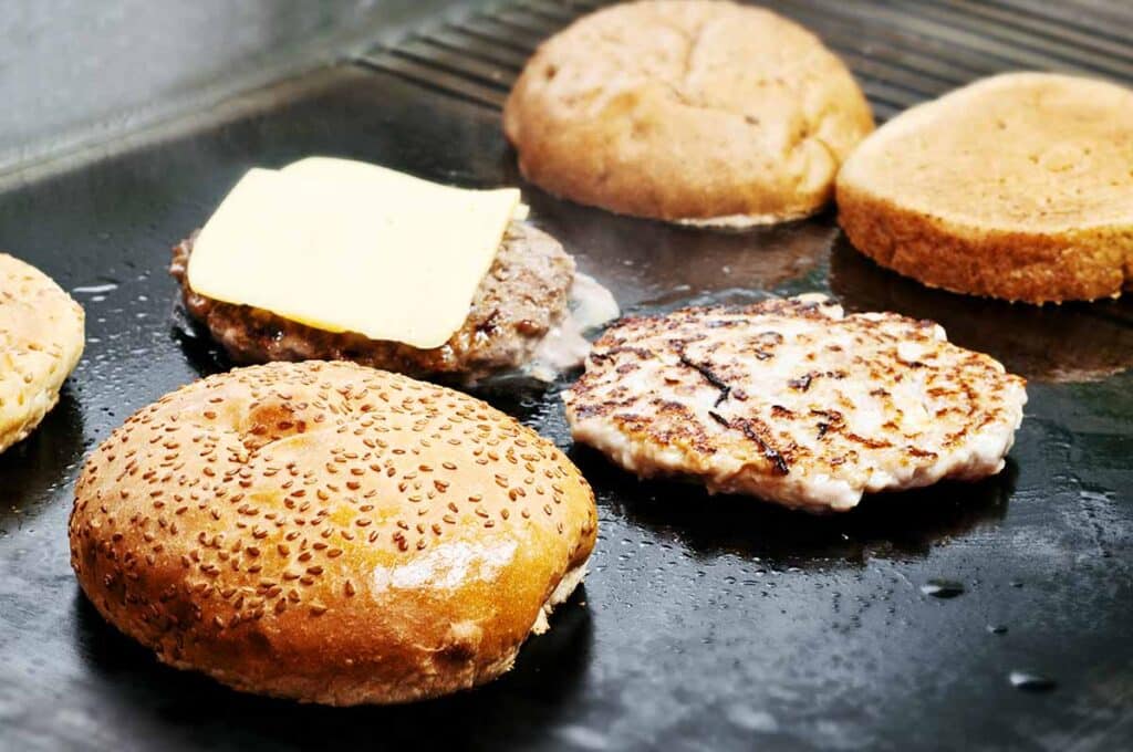 Grilling surface with hamburger patties and buns. 