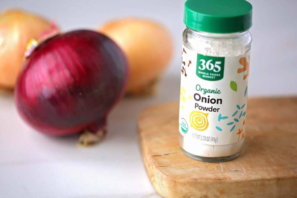 Bottle with onion powder next to whole onions. 