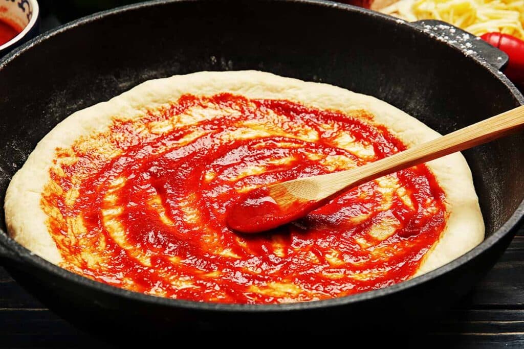 Cast iron skillet with pizza crust topped with pizza sauce. 