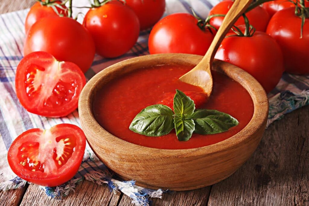 Wooden bowl filled with smooth tomato sauce and garnished with basil.