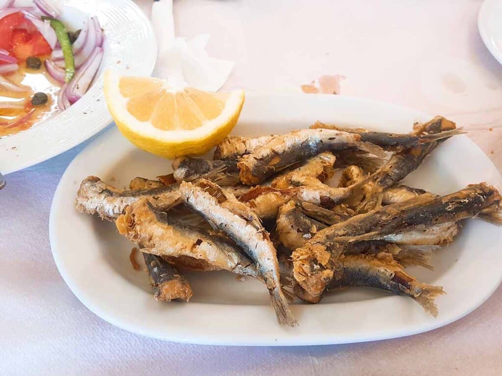 Plate with fried sardines with wedge of lemon next to it. 