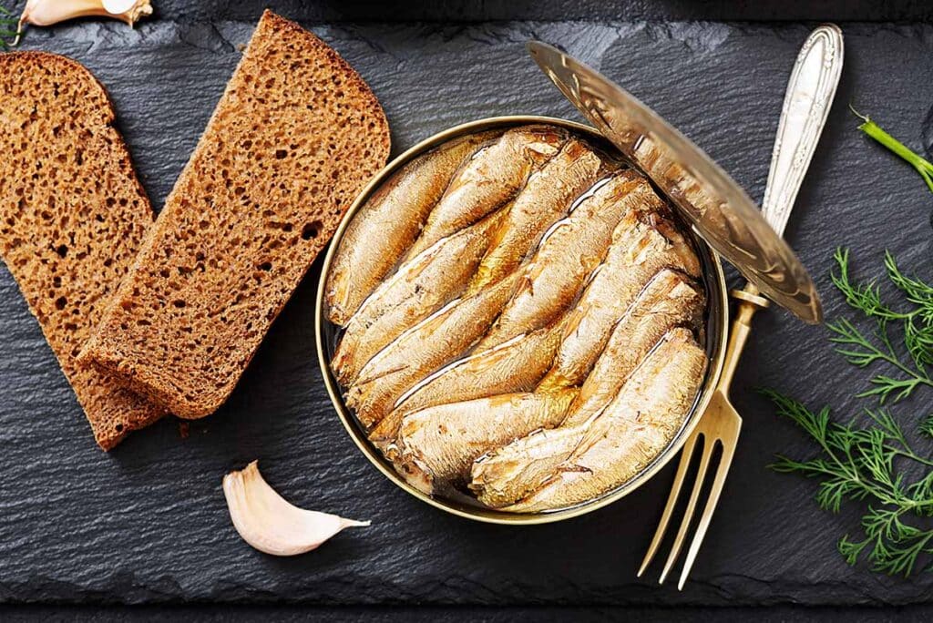 Round can with sardines and brown slice of bread next to it. 